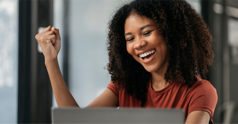 A woman happily smiles while working on her laptop.