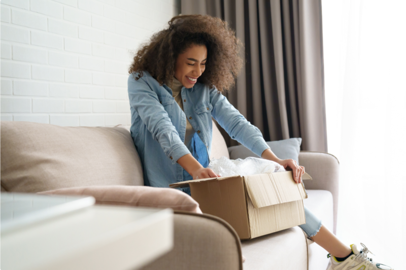 Woman sitting on couch opening a box.