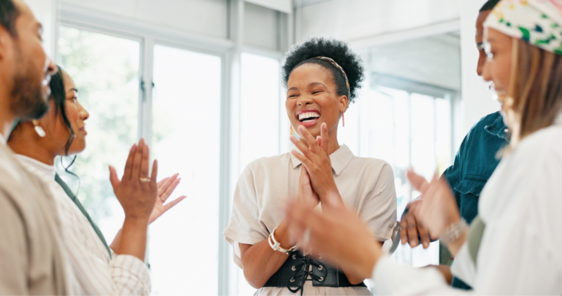 A diverse group of professionals clapping in unison in an office setting.