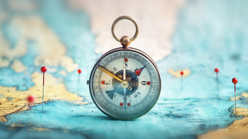 A vintage compass on a map with pins and pins on the world map.