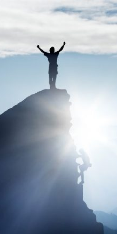 A man triumphantly stands atop a mountain, arms raised in celebration of his accomplishment.