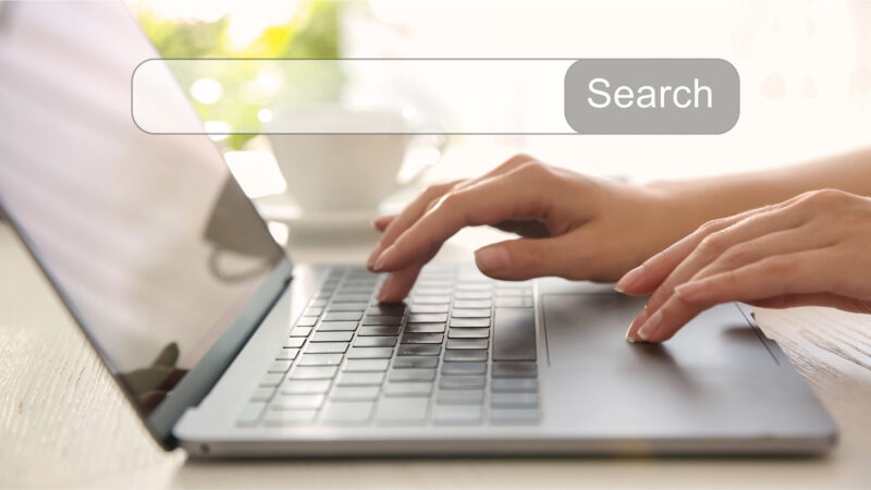 Person typing on laptop with word "search" displayed on screen.