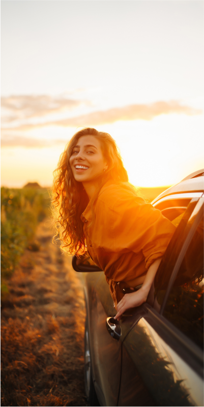 A woman leaning out of a car window, enjoying the sunset.