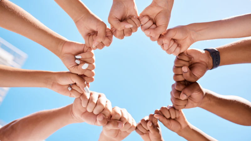 Group of hands creating a circle under a clear blue sky.