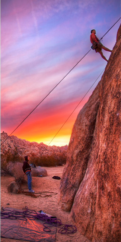 Silhouetted man ascending a rope during sunset.