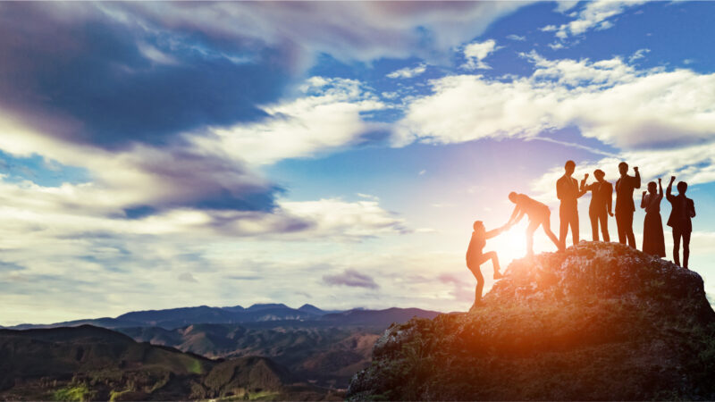 Group of professionals standing triumphantly on mountain peak, symbolizing success and teamwork.
