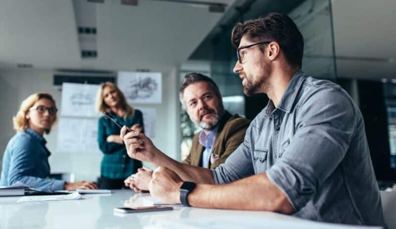 Two men and two women sit in a conference room and are talking about an automotive deal.