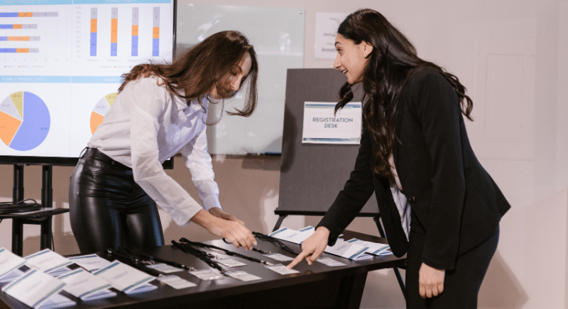 Two women are getting registered for an event at a registration desk.